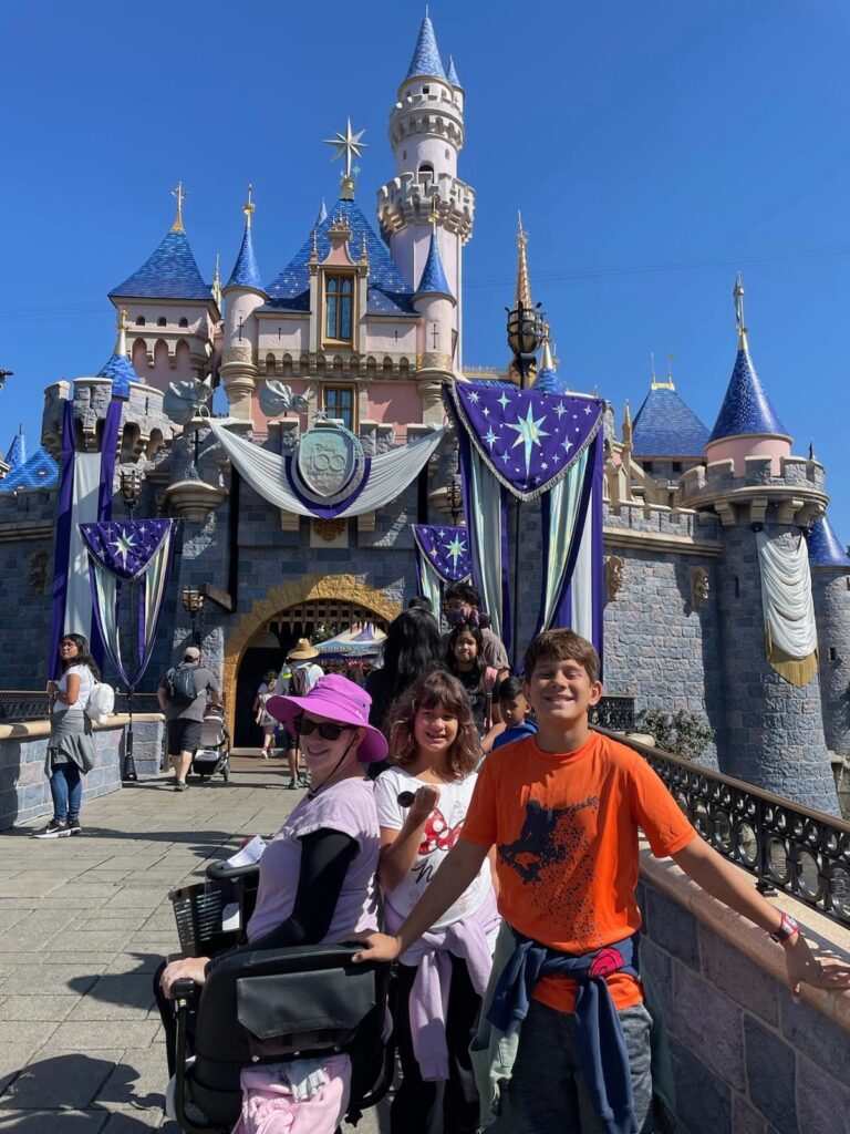 About US mom and 2 kids in front of disneyland castle with mom on scooter
