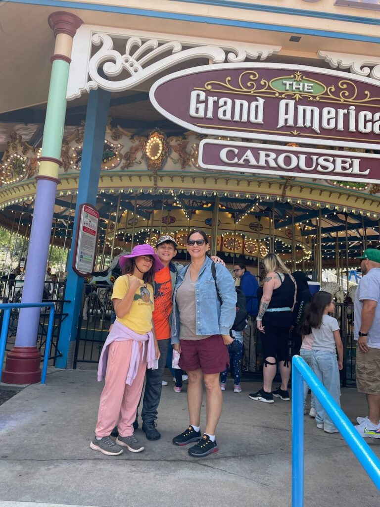 grandma and 2 kids standing in front of six flags grand carosel