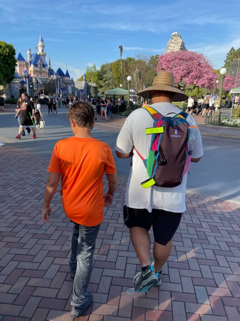dad in backpack and hat walking with son in disneyland